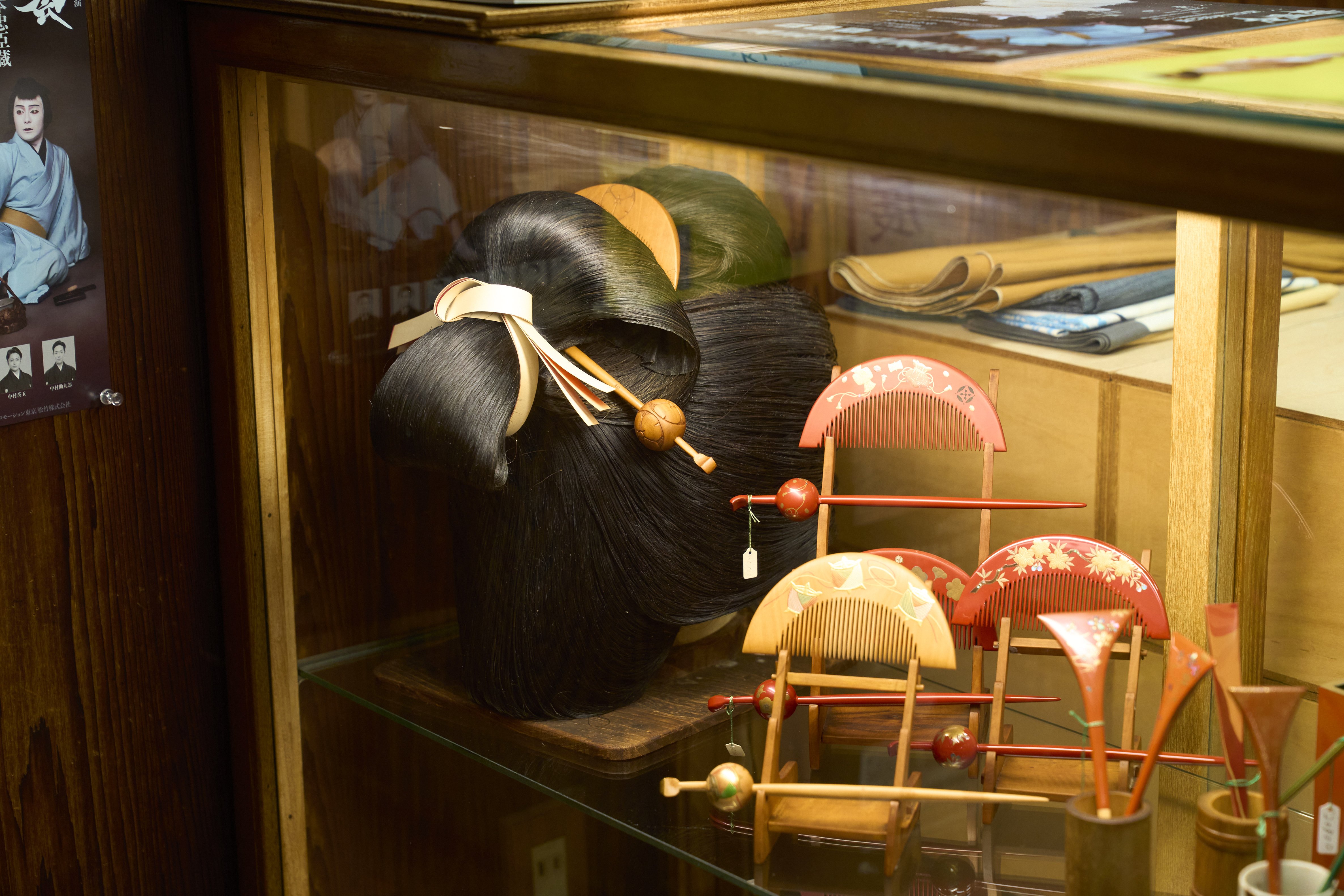 A display pairs combs and kanzashi with an Edo-period hairstyle model, illustrating the elaborate traditions of Japanese hairdressing.